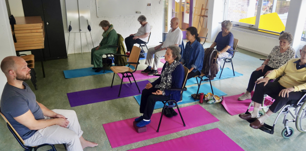 Man geeft Stoelyoga in Mariahoeve aan meerdere ouderen