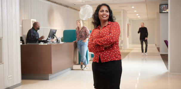 Collega van Staedion poseert bij de receptie van Staedion. Baliemedewerker is op de achtegrond in gesprek