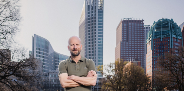 Projectmanager leefomgeving Stephan staat met armen over elkaar en kijkt in de camera. Op de achtergrond de skyline van Den Haag.