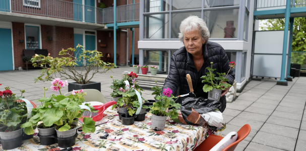 Mevrouw in de gezamenlijke tuin aan het werk met plantjes en bloemen.