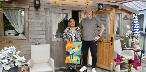 Een meneer en mevrouw poseren voor hun huis met een schilderij in de handen