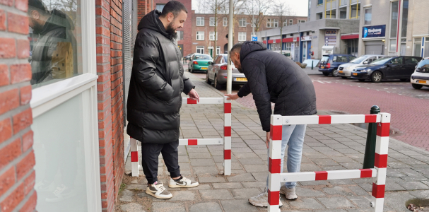 Twee mannen op straat aan het kijken naar een rood met wit hekje.