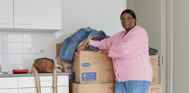 Mevrouw de Lannoy in haar nieuwe huis. Ze staat voor een stapel verhuisdozen.