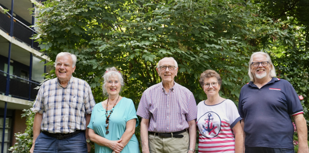Vijf leden van de bewonerscommissie poseren voor een groene boom voor het gebouw