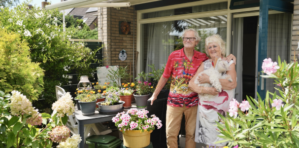 Cas en Carla met haar hondje in haar armen staan in hun tuin vol bloemen