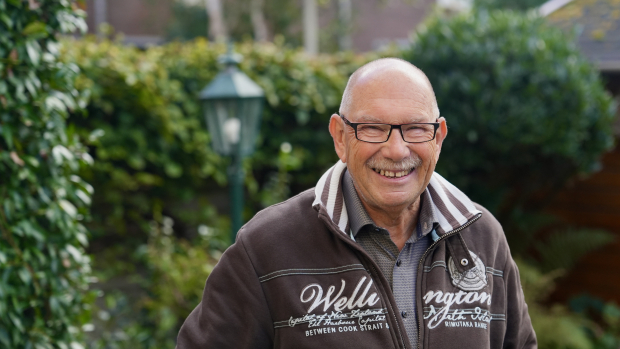 Henk staat in zijn tuin met een groene heg achter hem