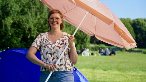 Killian met parasol in haar handen voor een blauwe tent