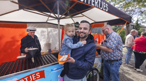 Buurtfeest burgemeester scholvinckplein: een man met kind op zijn arm bij de poffertjeskraam