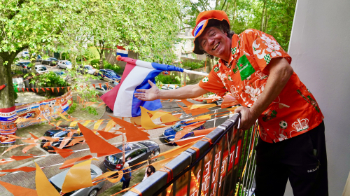 Michel in oranje t-shirt wijst naar oranje vlaggetjes bij zijn balkon