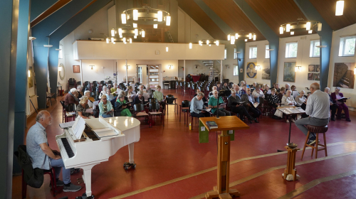 Samen repeteren: man achter witte piano en koor op de achtergrond