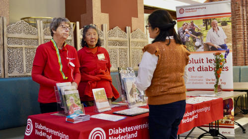 Infomarkt twee medewerkers van het diabetes fonds achter een stand in gesprek met een dame