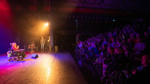 Optreden van vrouw in rolstoel met publiek dat toekijkt tijdens Regentes talentenshow 