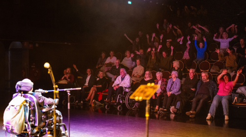 Optreden van vrouw in rolstoel met publiek op de achtergrond tijdens Regentes talentenshow 
