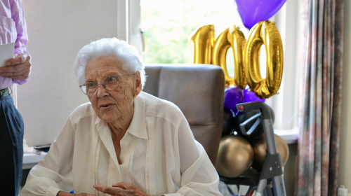 Albertje 100 jaar in een stoel met ballonnen op de achtergrond 