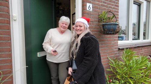 Medewerkers van Staedion delen kerstkransjes uit aan bewoner in deuropening