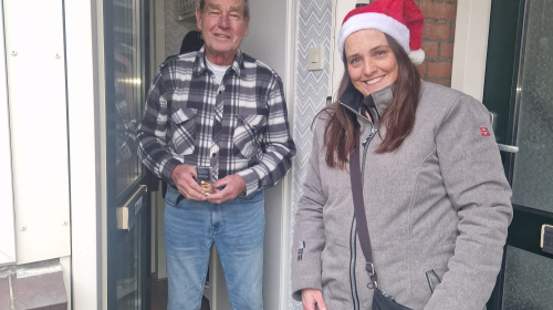 Mederwerker van Staedion deelt kerstkransje uit aan bewoner die in deuropening staat