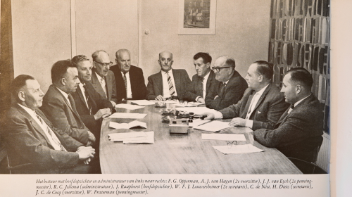 Een zwart wit foto van het oud bestuur samen rond de tafel
