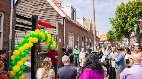Groep mensen kijkend naar de iemand die wat verteld onder een boog ballonnen