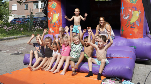 Blije kinderen tijdens het buurtfeest op het springkussen met hun handen in de lucht
