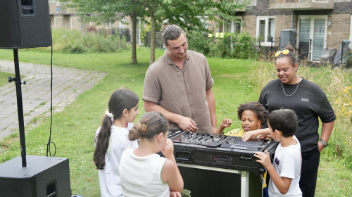 Kinderen draaien aan de knoppen van de draaitafel onder toeziend oog van de DJ
