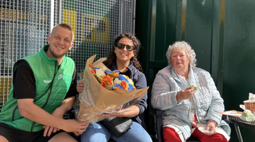 Wijkconsulent van Staedion krijgt een bos bloemen voor de 25e verjaardag van Staedion van medewerkers van Haags Hopje aan het Oranjeplein