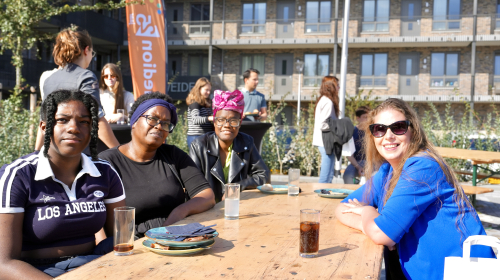 Alle buren samen. Op de achtergrond een groep in gesprek en aan tafel drie vrouwen