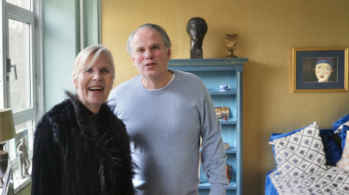 Saskia en Ad staan naast elkaar in de woonkamer voor een gele muur en blauwe kast