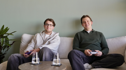 Twee vrienden met game controllers in hun handen op de bank.