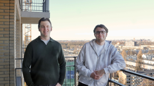 Twee Friends samen op hun balkon met de stad op de achtergrond.