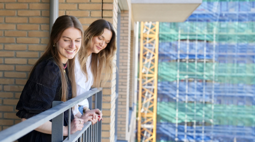 Twee meiden kijken over de rand van hun balkon