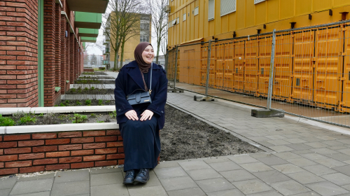 Bewoonster van de nieuwe woningen zit voor haar nieuwe huis op een muurtje