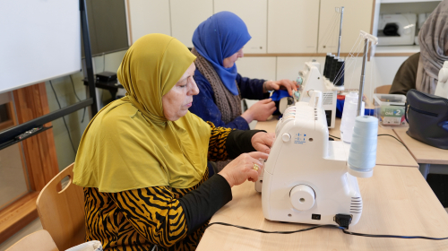 Twee dames krijgen naailes, ze zitten achter de naaimachine