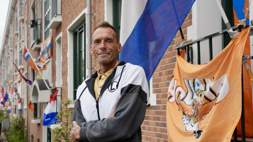 Mike in de van Ruysbroekstraat tussen de oranje en Nederlandse vlaggen voor het WK