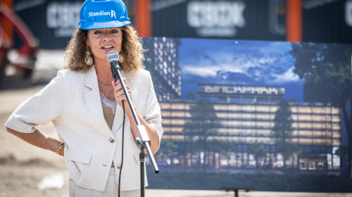 Miriam achter de microfoon voor het bouwbord van de Binckhorts 