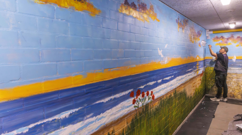 Lokale kunstenaar en Staedion-huurder Cor Wakum werkt aan een nieuwe muurschildering in de corridor tussen Landzicht en Cardia