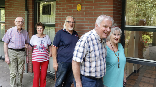 De vijf leden van de bewonerscommissie lopen naar de entree van het woongebouw