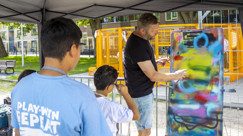 Een man geeft uitleg over graffiti spuiten bij het evenement 'Wereldwijk Schilderswijk'