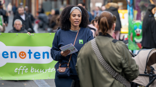Een vrouw deelt folders uit aan bewoners