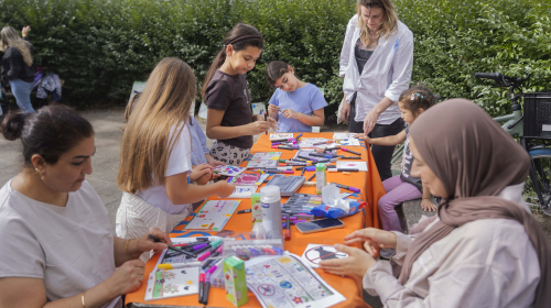 Kinderen maken samen met volwassenen tegeltjes voor in de binnentuin.