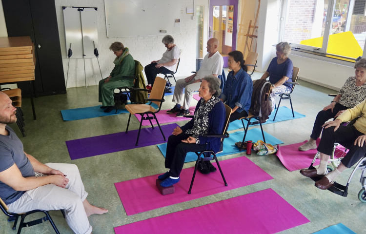 Man geeft Stoelyoga in Mariahoeve aan meerdere ouderen