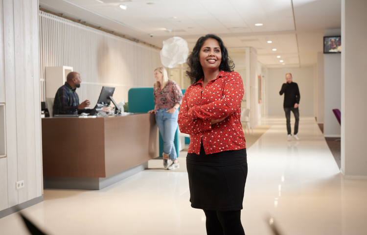 Collega van Staedion poseert bij de receptie van Staedion. Baliemedewerker is op de achtegrond in gesprek