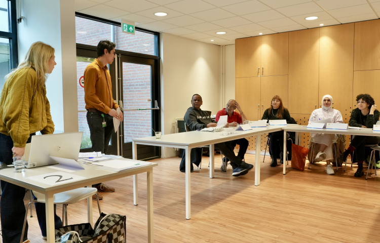 workshopleider Carin geeft workshop en staat voor een aantal bezoekers die aan tafel zitten