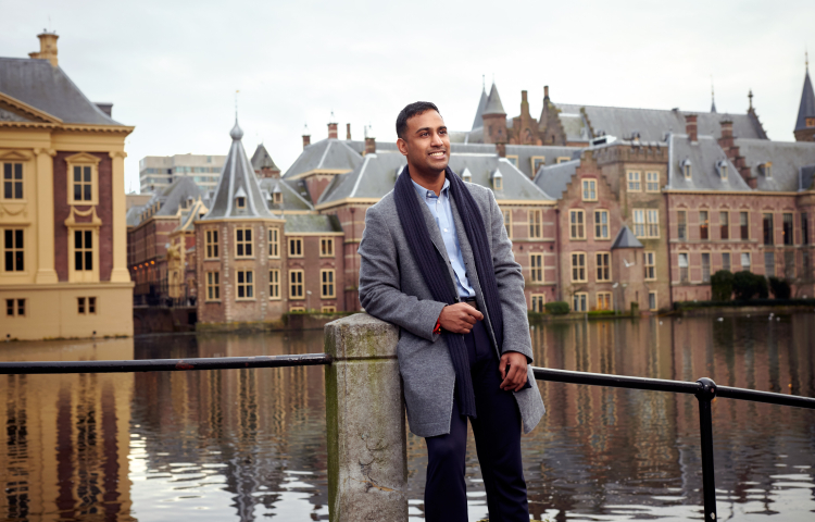 Man leunt tegen een hek aan, voor het water.