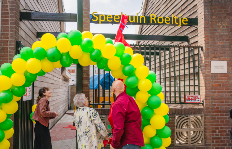 Twee dames en meneer onder een boog ballonnen en onthullen bord met naam Speeltuin Roeltje