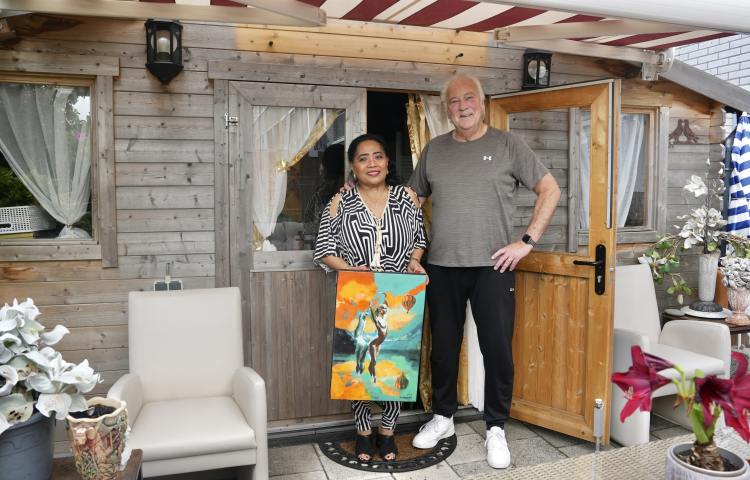 Een meneer en mevrouw poseren voor hun huis met een schilderij in de handen