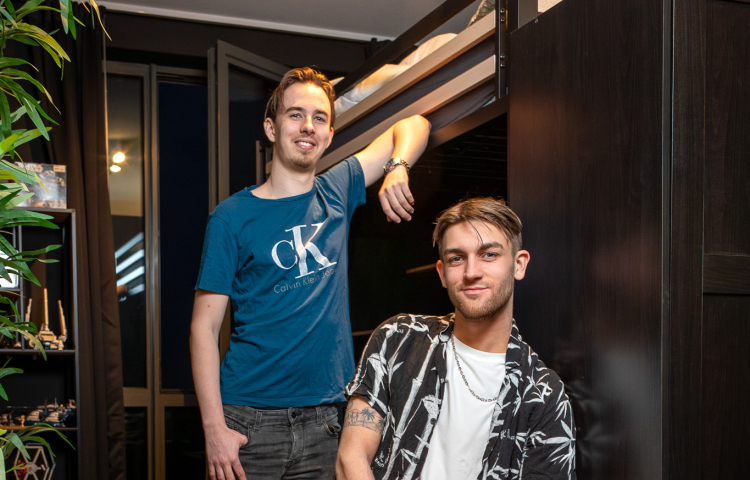Twee jongens, een zit op een kruk en de ander staat met zijn arm tegen de muur aan