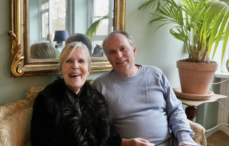Buurvrouw Saskia en Buurman Ad zitten samen op een bank en lachen breeduit