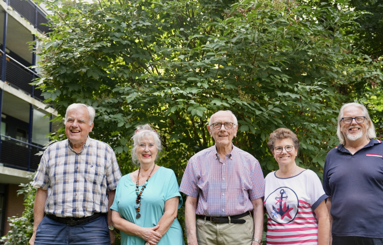 Vijf leden van de bewonerscommissie poseren voor een groene boom voor het gebouw