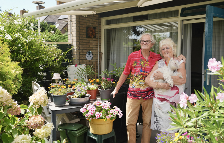 Cas en Carla met haar hondje in haar armen staan in hun tuin vol bloemen