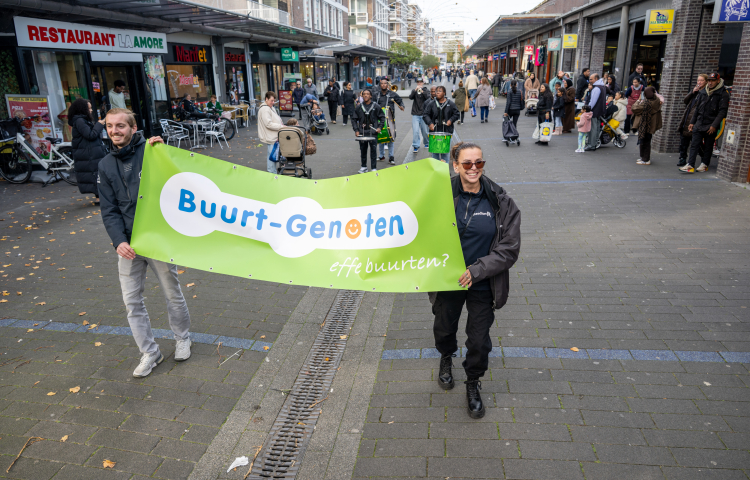 Een man en een vrouw lopen met een vlag waarop Buurt-Genoten staat.